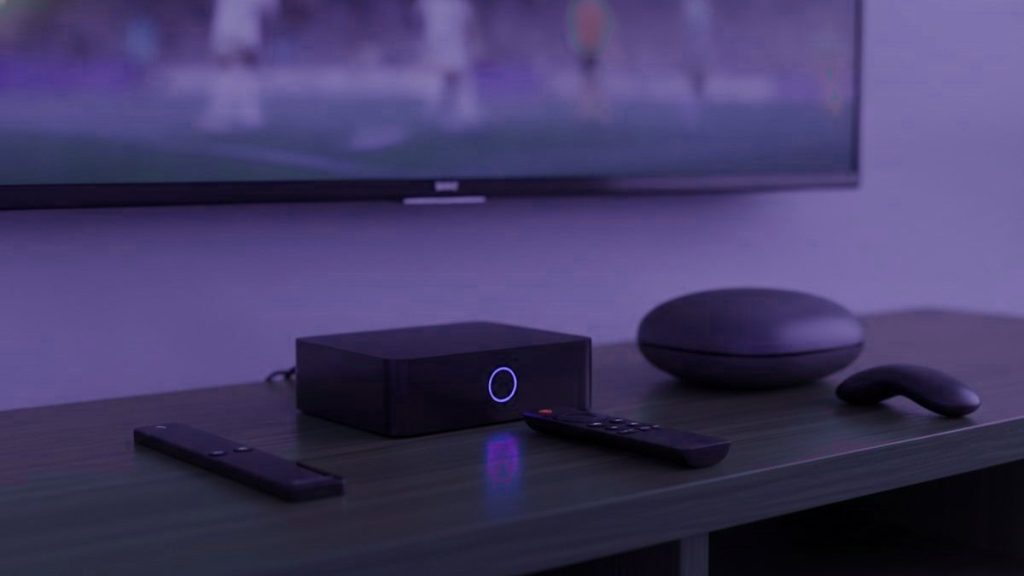 A streaming stick, a set-top box and a round streaming box with their remotes on a TV console