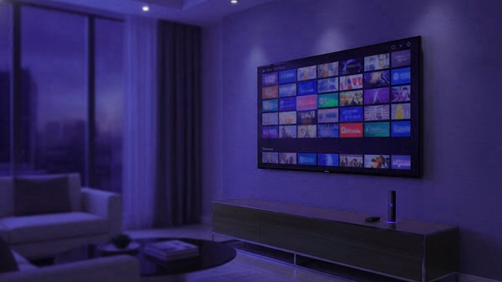 A living-room TV showing an IPTV channel guide with a streaming stick on the console